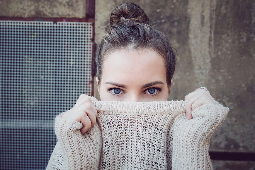 Woman with blue eyes hiding face in beige knit sweater