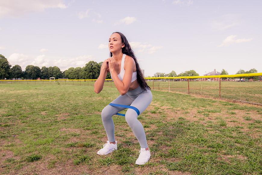 Woman performing resistance band squat exercise outdoors
