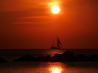 Silhouette of sailboat on ocean during vibrant orange sunset