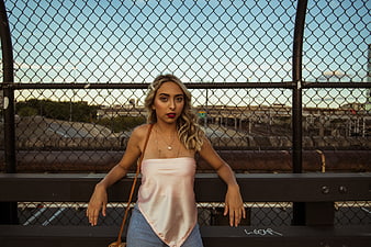 Blonde Woman in Pink Top Leaning on Urban Fence