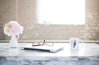Minimalist workspace with laptop, flowers, and coffee mug on marble