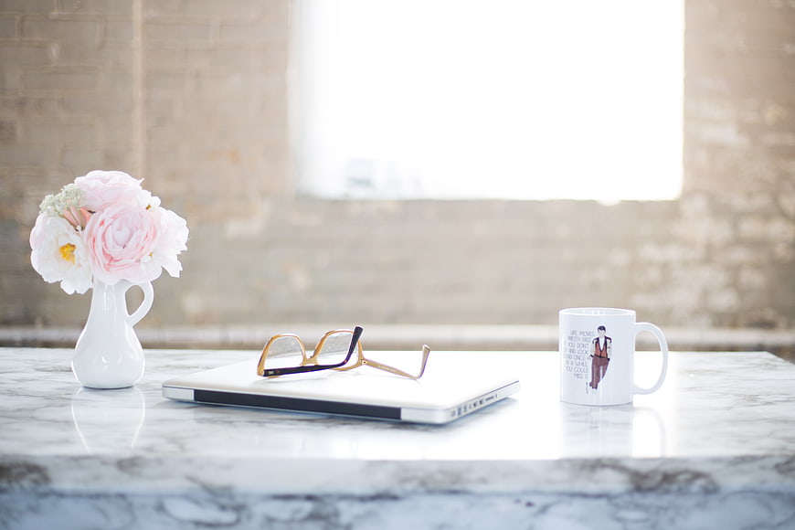Minimalist workspace with laptop, flowers, and coffee mug on marble