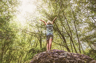 Young woman standing on rock in forest with arms raised