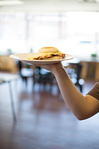 Hand holding breakfast sandwich on white plate in cafe