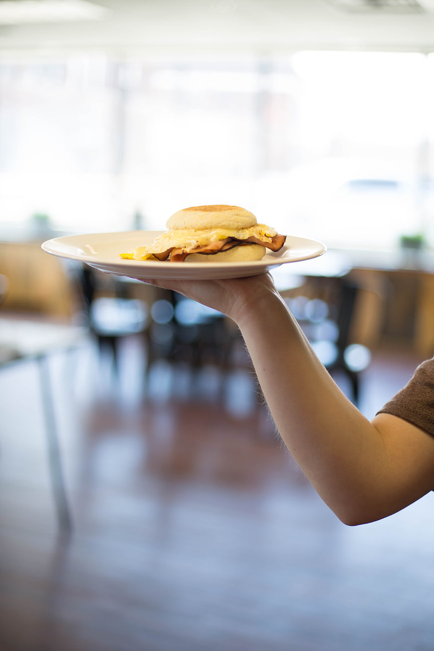 Hand holding breakfast sandwich on white plate in cafe