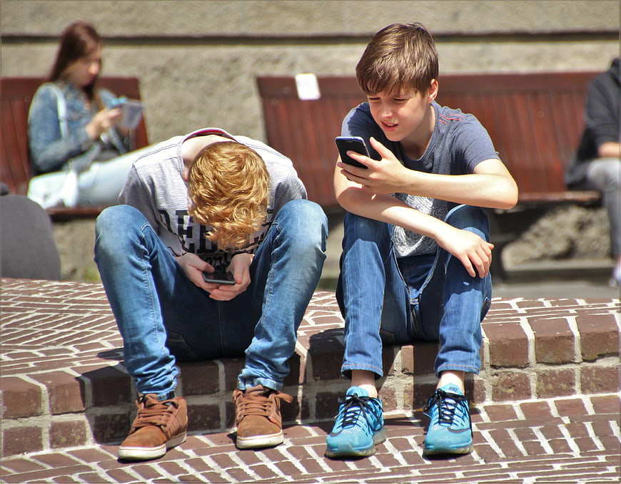 Two boys sitting on brick steps using smartphones outdoors