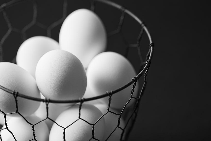 White eggs in wire basket on dark background