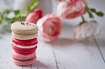 Stack of colorful macarons with pink flowers on white wood