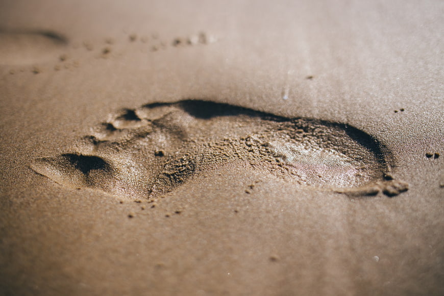 Close-up of a single footprint in wet sand on a beach