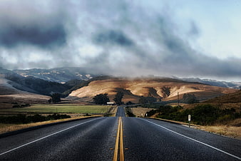 Winding asphalt road through rolling hills under dramatic clouds