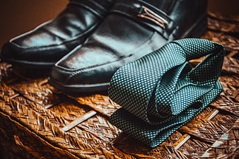 Black leather loafers and patterned tie on woven surface