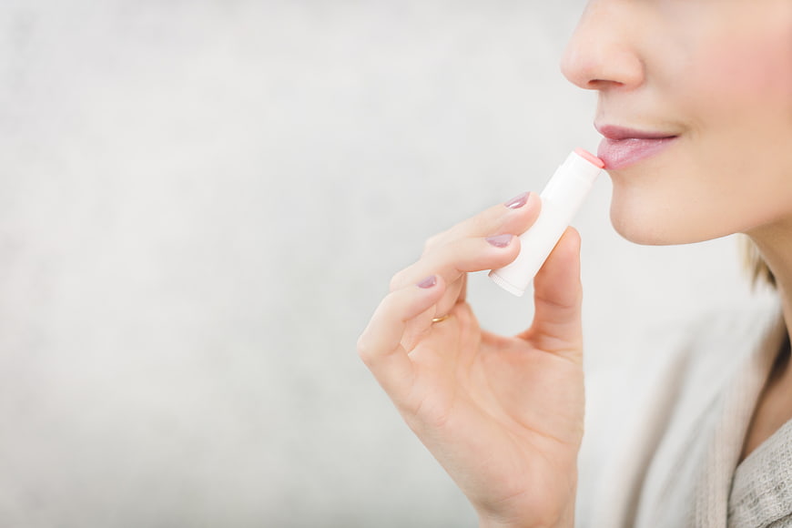 Woman applying lip balm on white background