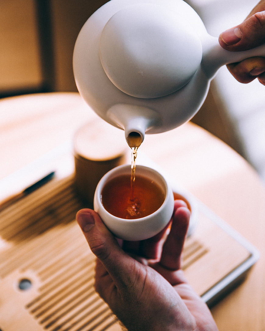 Pouring Tea from White Teapot into Cup