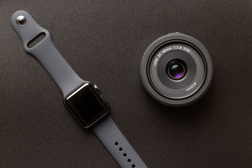 Smartwatch and Camera Lens Flat Lay on Dark Textured Surface