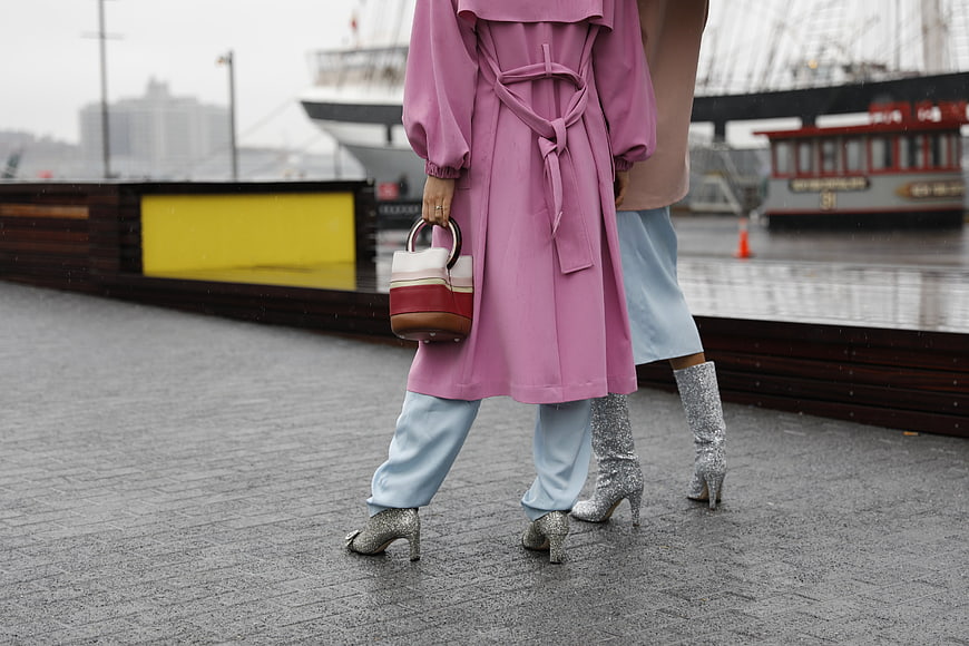 Two women in pink coat and silver boots walking on wet pavement